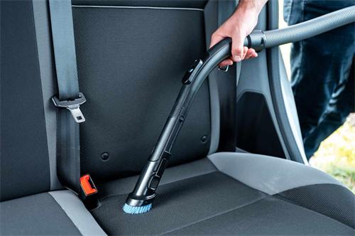 Close-up view of a hand using a vacuum cleaner brush attachment to clean fabric car back seats