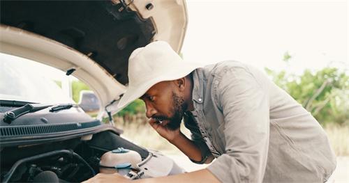 "A man making a phone call while inspecting the engine of his broken-down car on the roadside"