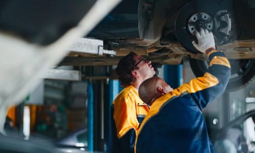 "Two auto mechanics inspecting the brake disc of a car lifted on an automotive lift in a repair garage"