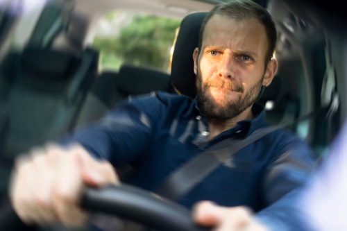 "Stressed male driver gripping the steering wheel tightly while driving a vehicle on the road"