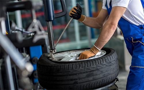 "Auto repair technician working to dismount a car tire from its alloy wheel at a service station"