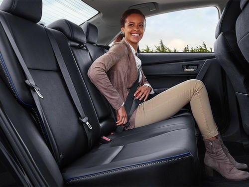 "Smiling woman fastening her safety belt while sitting on a car's black leather rear seat"
