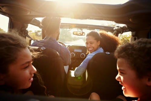 "Happy family traveling together inside an open-top off-road vehicle on a sunny day"