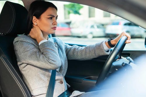 "Female driver suffering from neck discomfort while holding her painful neck during driving"