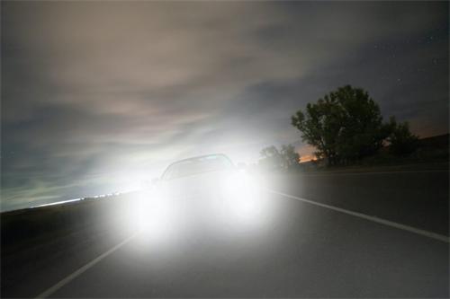 "Oncoming car with extremely bright high beam headlights traveling on a rural road at dusk"