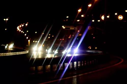 "Bright vehicle headlights producing lens flare on a wet urban overpass at night"