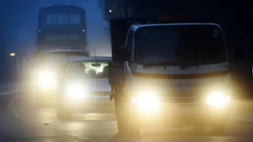 "Vehicles with dazzling high beams causing glare and poor visibility driving on a foggy road at night"