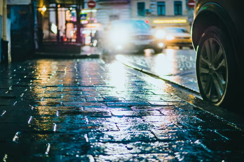 "Wet city street reflecting dazzling vehicle headlights on a rainy night in town"