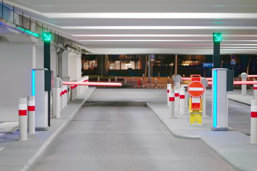 "Entrance barrier gate system of an underground parking lot with green traffic indicator lights and safety bollards"