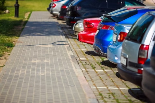 "Multiple cars neatly parked in marked outdoor roadside parking spaces beside a sidewalk and lawn"