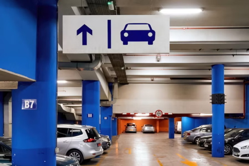 "Indoor underground parking garage with blue support pillars, directional parking sign and various parked vehicles"