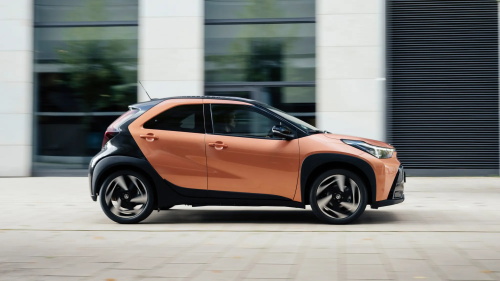 "Orange and black two-tone compact crossover SUV driving on paved ground in front of a modern glass building"