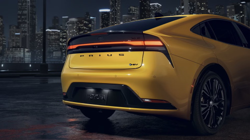 "Rear view of a yellow Toyota Prius hybrid sedan parked on a city waterfront at night with illuminated taillights"
