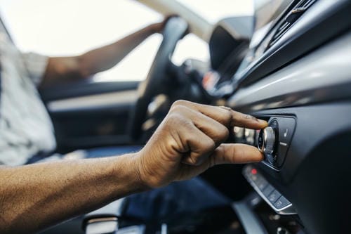 "Close-up of a driver’s hand turning the control knob on a car dashboard to adjust vehicle settings