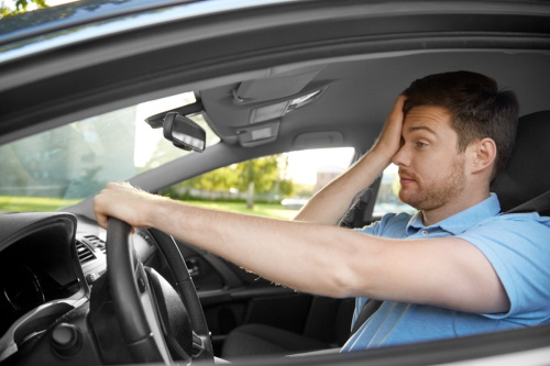 "Stressed male driver resting one hand on his forehead while holding the steering wheel, showing driving anxiety and fatigue"
