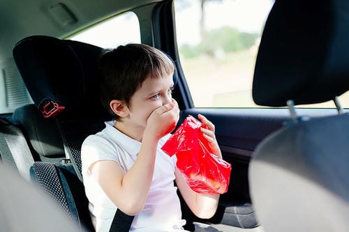 "Little boy suffering from motion sickness covering his mouth while holding a plastic bag in a child safety seat inside a car"