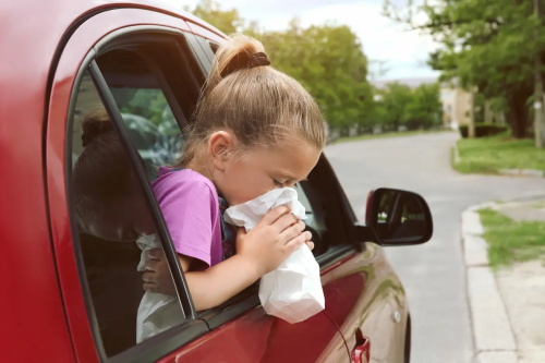 "Little girl leaning out of a car window getting carsick and vomiting into a tissue during a road trip"