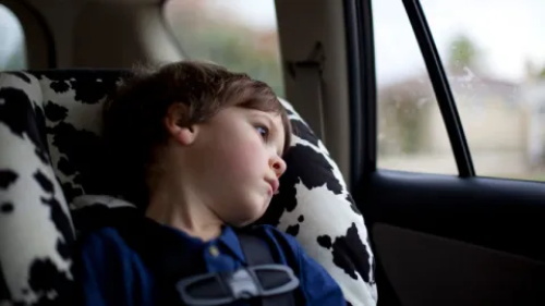 "Young boy sitting safely in a child safety car seat in the back of a vehicle, looking tired and sleepy"