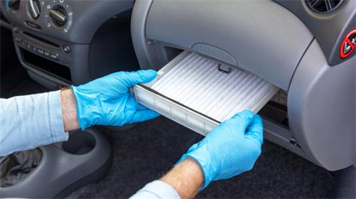 "Mechanic installing a new clean cabin air filter behind the car glove compartment while wearing protective blue gloves"