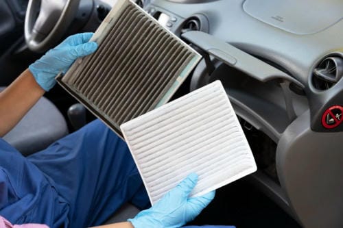 Technician wearing blue gloves comparing a dirty old car cabin air filter with a clean new replacement inside a vehicle" 图片 2
