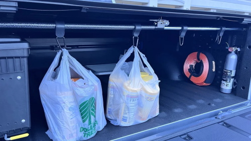 "Pickup truck trunk equipped with hanging storage rods, two shopping plastic bags hung on hooks, with a tool box, fire extinguisher and tow rope placed inside the cargo compartment"