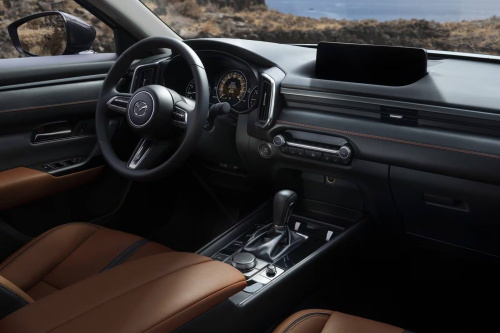 "Mazda interior with a minimalist design, equipped with a suspended small central screen, physical knob controls, brown leather seats and a traditional automatic gear shift lever"