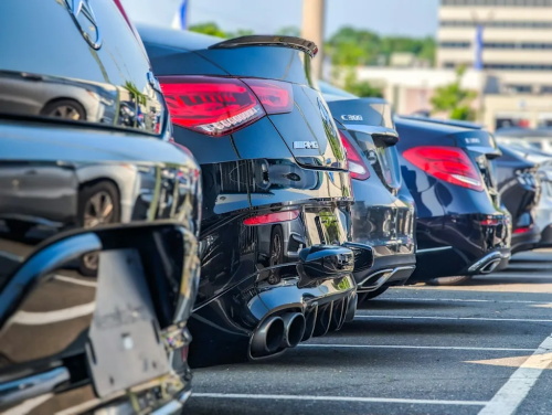 Rear view of a row of premium Mercedes-Benz AMG performance vehicles parked in a dealership lot, featuring sporty quad exhaust pipes and high-performance rear styling.