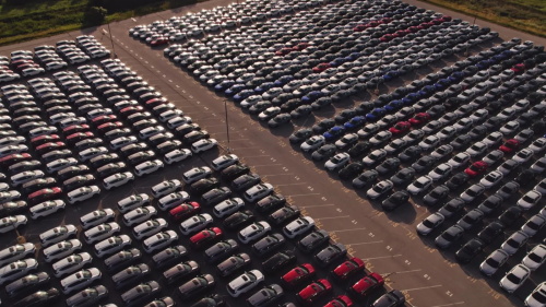 Aerial shot of a large finished vehicle storage yard, with massive quantities of new cars neatly parked in rows, serving as the transit inventory warehouse for automobile manufacturers before delivery to dealerships.