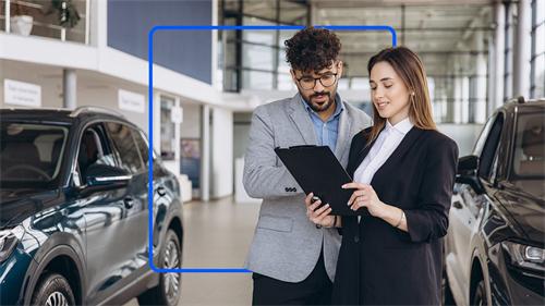  A professional auto sales consultant introduces vehicle parameters and purchase terms to a customer with a document folder in a 4S car showroom.
