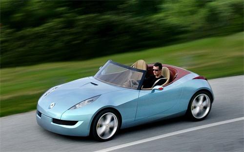 "Man driving a light blue Renault two-seater convertible sports car on an asphalt road surrounded by green countryside scenery"