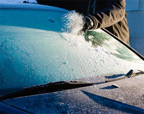 "Person sprinkling de-icing salt on a thick layer of frost covering a car windshield on a cold winter morning"