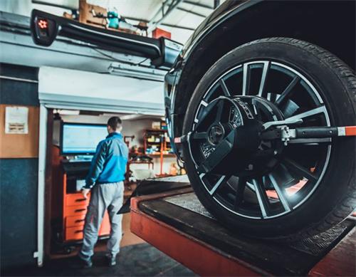"Auto repair technician performing 3D wheel alignment on a lifted vehicle in a garage workshop"