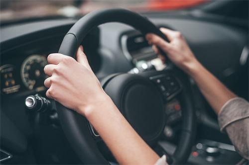 "Close-up of driver's hands gripping a black leather car steering wheel while driving"
