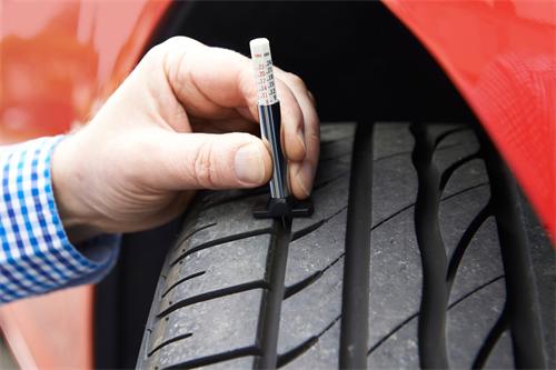 "Mechanic using a tread depth gauge to measure the remaining tread on a car tire"