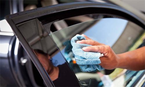 "Hand wiping a car side window clean with a blue microfiber cloth"